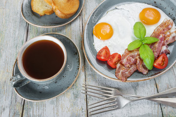 Fried eggs,  bacon, tomato, toast and a cup of coffee