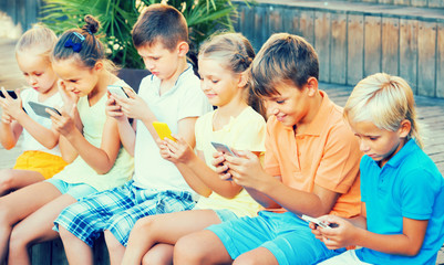 Group of cheerful kids playing with mobile phones outdoors