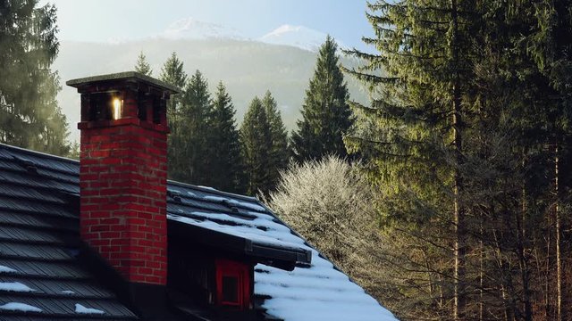 Chimney on small cottage house in winter forest, snow on the rooftop, evergreen trees in background