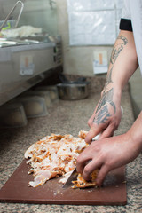 The chef in the cafe or restaurant prepares food in the kitchen, only the hands, he cuts meat or steak knife on the board for the food on the plate. Cooking.