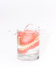 Two acrylic dentures immersed in a glass of water,white background.