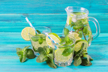 Mojito with mint and lime in a glass and a jug with tubes. Blue wood background.