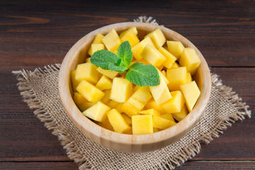 Tropical fruit mango in a plate on a wooden background, whole or sliced.