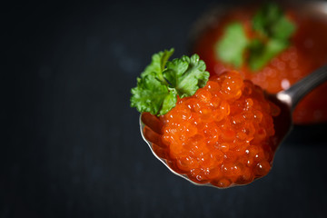 Red caviar decorated with parsley in silver spoon on a dark background, selective focus