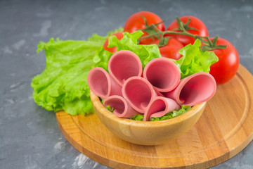 Sliced sausages with salad leaves on the wood background