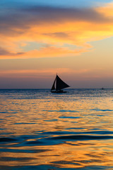 Naklejka na ściany i meble Traditional sailing boat and a tropical sunset on a calm ocean