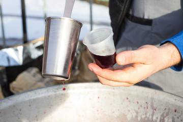 Fototapeta na wymiar Street food: in the hand of plastic cup with mulled wine, metal ladle and cooking pot