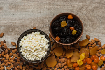 cottage cheese in white plate and the prunes in the brown plate. Prunes, dried apricots, dried mandarins and almonds on a light wooden background