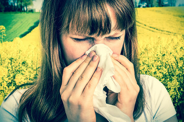 Woman with allergy on yellow rape field sneezing in tissue