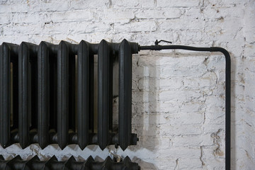 Old black cast iron radiator on a white brick wall