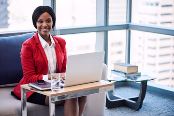 Black female businesswoman smiling at the camera while seated on a couch in a business lounge with...