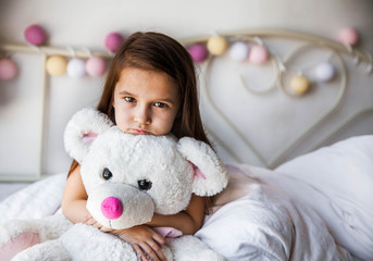 Little girl with her teddy sitting on the bed. home, comfort, family, relationships, people