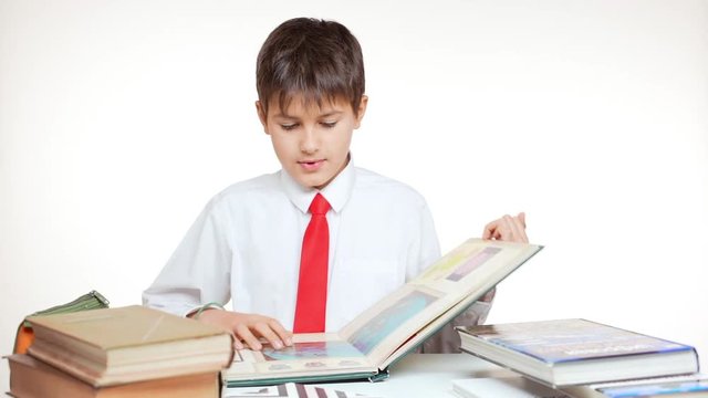 Young confident school kid in red tie sitting at table folding pages of book on white background in slowmotion