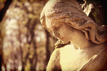 Vintage image of a sad angel on a cemetery against the background of leaves