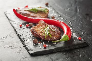 grilled steak with rosemary and chili pepper on dark stone
