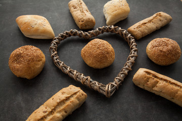Concept of gluten free buns for allergic people with disease. Variation of bread with wooden heart shape on dark background.