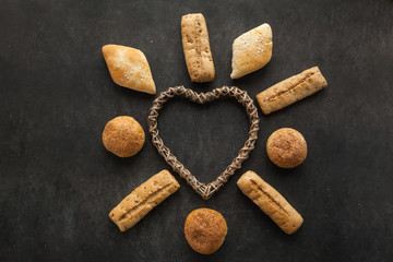 Concept of gluten free buns for allergic people with disease. Variation of bread with wooden heart shape on dark background.