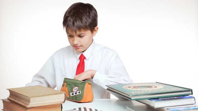 Young concentrated school kid with red tie sitting at table with books and seeking chancery in pen case in slowmotion