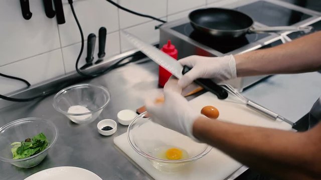The cook breaks egg in a glass bowl.
