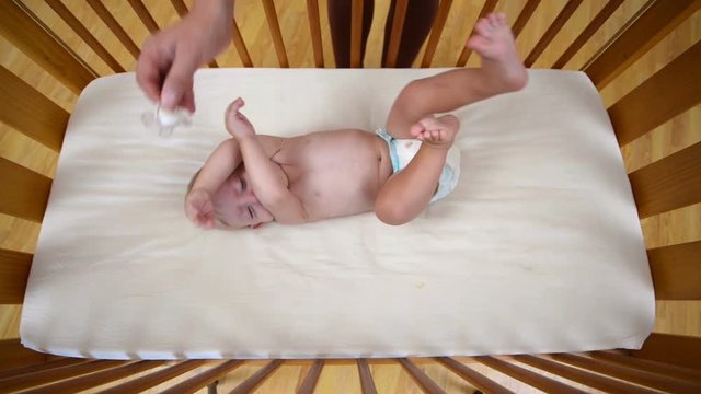 Baby crying in crib at home and being caressed by his mother