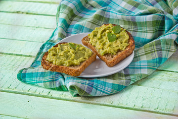 toasts with avocado paste and parsley on green background, checked tablecloth on the side