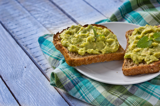 Sandwiches with avocado paste on white boards and green checked tablecloth