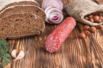 salami, bread, garlic, onion, hazelnuts in a linen pouch and dill on an old wooden table.
