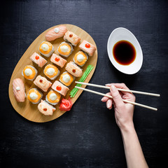 Fototapeta na wymiar Sushi rolls and sauce and hand with chopsticks on a dark background. Traditional Japanese food. Top view. Flay lay