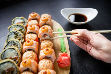 Traditional Japanese food - sushi rolls, sauce and hand with chopsticks on a dark background.