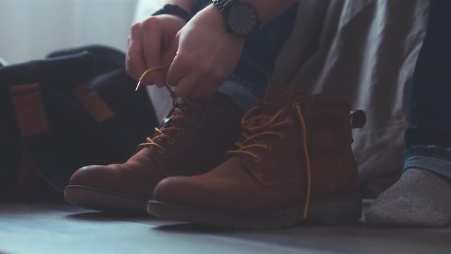 CU Caucasian male tying shoelaces on his brown leather shoes while sitting on bed. 50FPS SLO MO 4K UHD RAW edited footage
