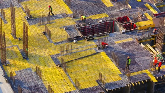 Top view of a group of construction workers at construction site. Builders laids metal reinforcements for the new floor slabs. Zoom out effect from the bottom point. Time lapse