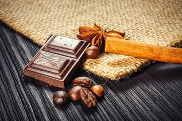 Chocolate bar and spices on wooden table, close up