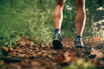Muscular calves of a fit male jogger training for cross country forest trail race in nature park.