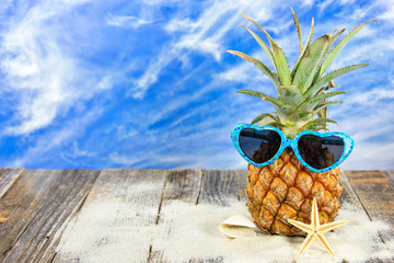 pineapple wearing heart shaped sunglasses in sand with starfish and seashell