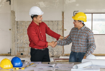 Architect engineer shaking hands other hand he is holding a helmet at construction site. With blueprint on table. - business teamwork, cooperation, success collaboration concept