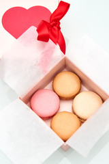 4 colorful macaroons wrapped in the Valentine's Day themed pink box with red heart and bow on top of the box.