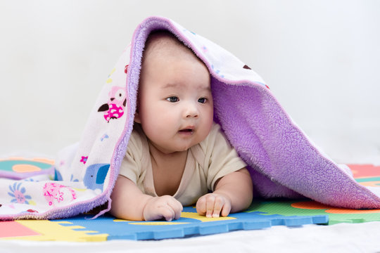 Portrait of a little adorable newborn infant baby girl with blanket and saliva lying on the tummy on colorful eva foam and looking forward indoors