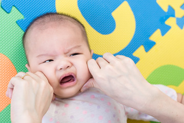 Parent pinch the cheeks a little adorable newborn infant baby girl that lying on the back on colorful eva foam indoors