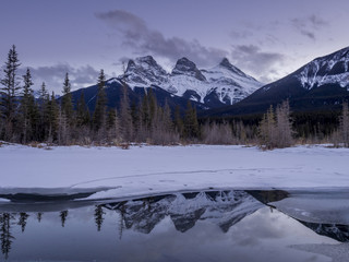 Sunset view of the Three Sisters from a frozen Policemen's Creek along the Bow River outside Canmore, Alberta in winter.