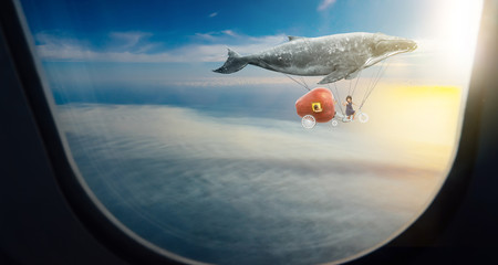 Whale floats in the air above the clouds carrying children in a yellow airplane,seen through window...