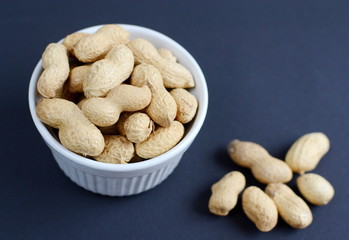 White bowl of peanuts. Black background