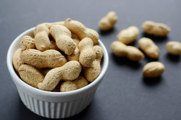White bowl of peanuts. Black background