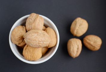 White bowl of walnuts. Black background