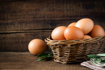 Fresh eggs in a rustic willow basket against dark wooden background
