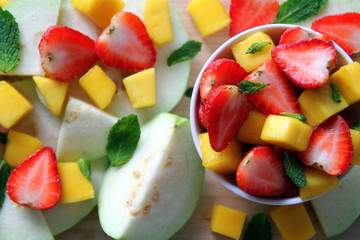 Fresh fruits – guava, mango and strawberry with leaves of mint on the wooden background.