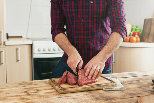 Man cuts of beef meat on a wooden cutting board