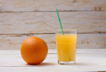 A whole orange with a glass of orange juice on a white wooden background.