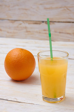 A whole orange with a glass of orange juice on a white wooden background.