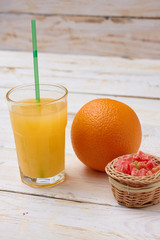 A whole orange with a glass of orange juice on white wooden background with candy in a plate.  Concept.