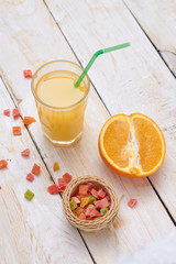 A whole orange with a glass of orange juice on white wooden background with candy in a plate.  Concept.